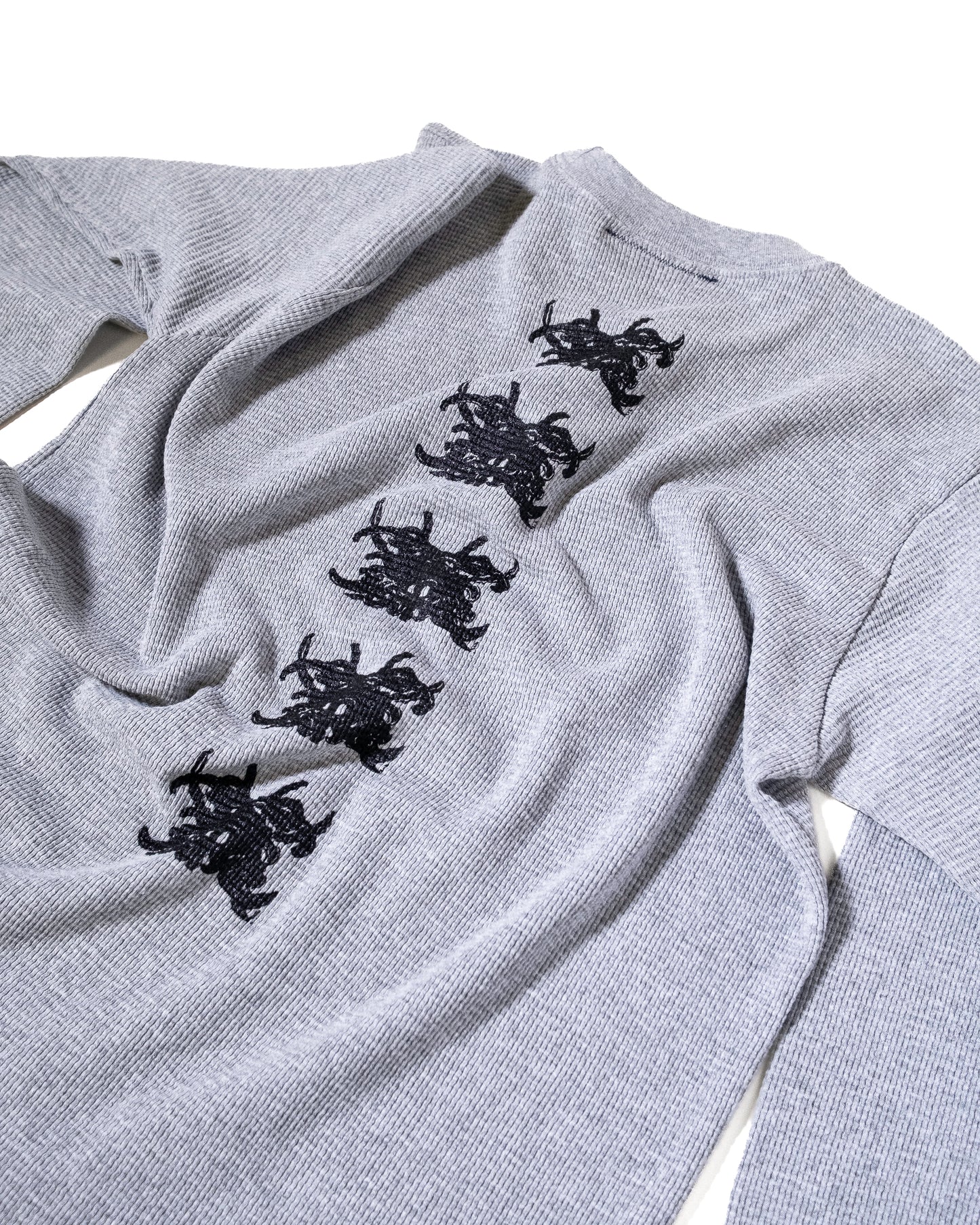 Gray sweater with black embroidered designs on a white background