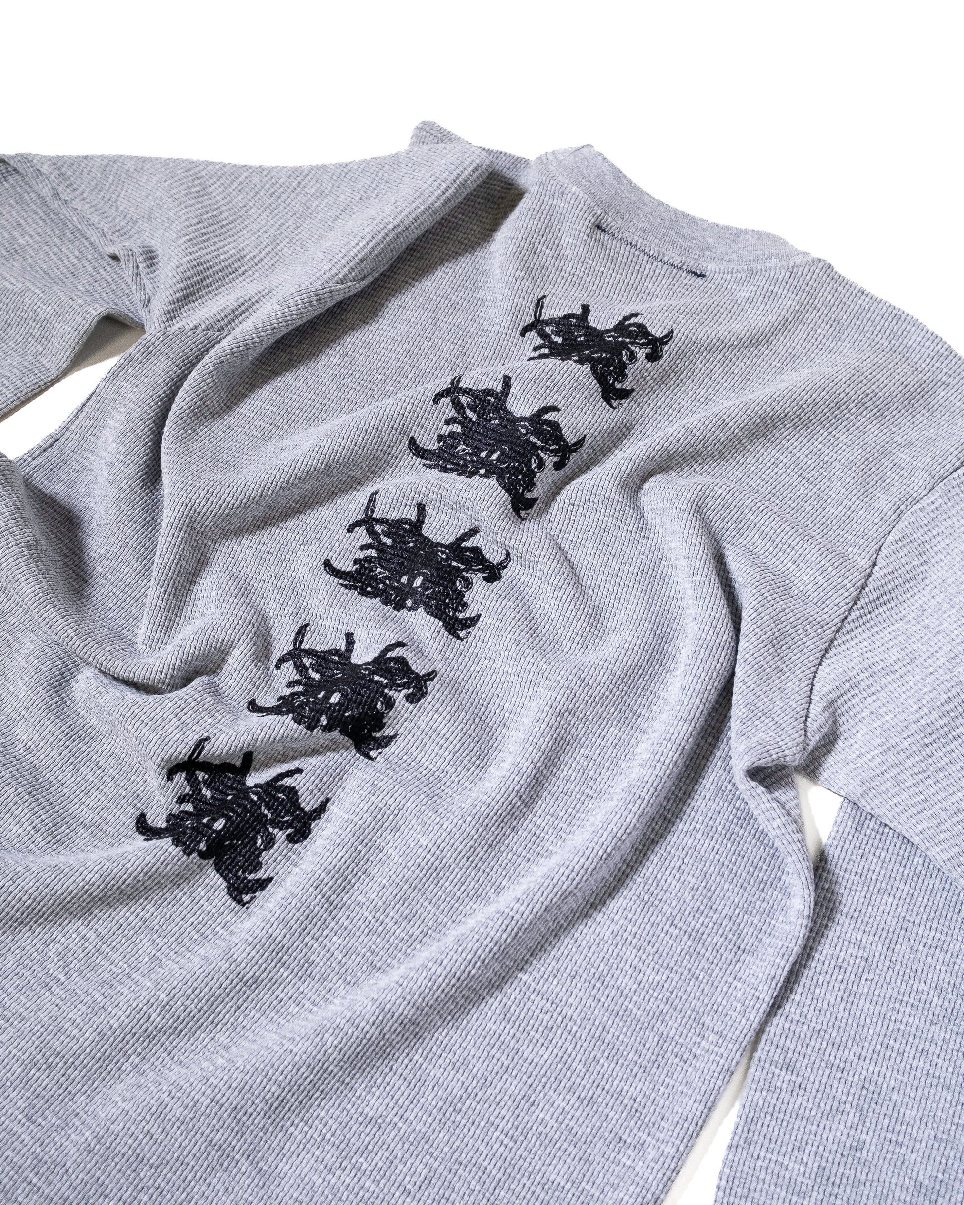 Gray sweater with black embroidered designs on a white background