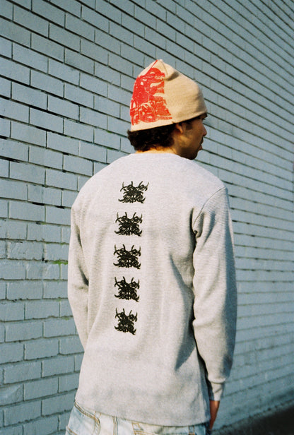 Person wearing a light gray long-sleeve shirt with black designs on the back, standing against a light blue brick wall.